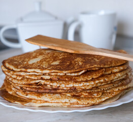 Stack of thin crepes, blini with butter on white plate. Maslenitsa, Shrove Tuesday concept. Vertical orientation, rustic style