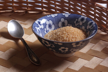 Brown cane sugar in a blue bowl on a wooden table close-up