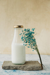 glass bottle of milk on natural stone stand and bouquet of blue dried flowers for decoration. eco storage of milk in reusable containers. tuse of natural materials for decoration. select focus