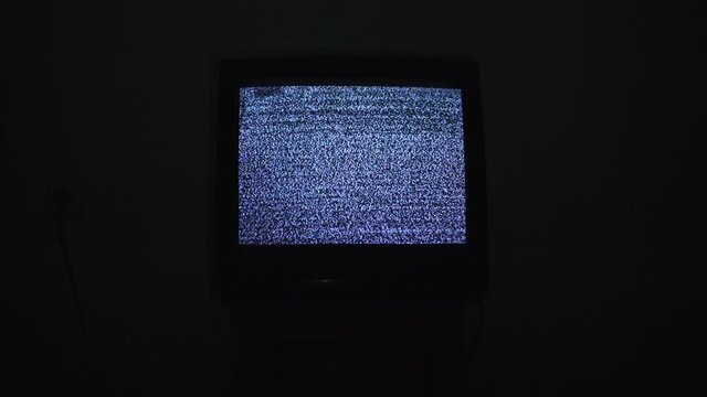 Broken tv screen with noise analog static signal in black room at night