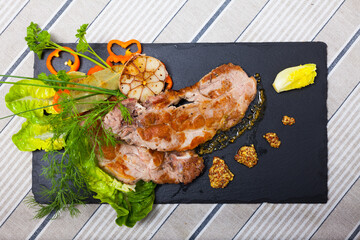 Image of cooked fried pork meat with different herbs served on black plate