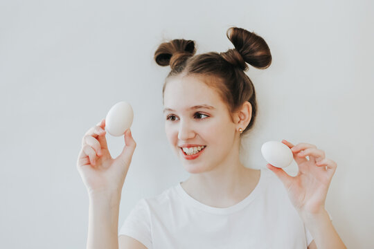 A cute happy teenage girl with bunny ears made of her hair holding white eggs in her hands. Kid ready for Easter hunt party, going to paint eggs. Happy Easter, holiday, childhood concept.