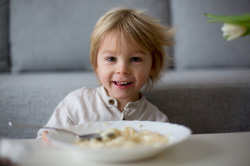 Cute toddler boy, eating pasta with white cheese at home