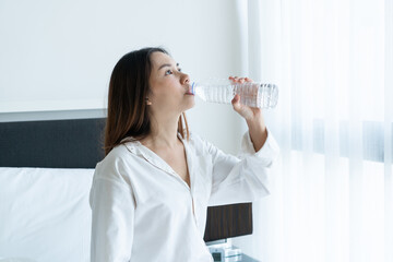 Happy smiling young Asian female drinking water after waking up in the morning. Healthy, beauty, diet concept.