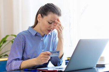 Upset young woman holding head, using laptop, online banking service, problem with blocked credit card, irritated girl checking balance, internet fraud concept, bankruptcy, debt, overspend, finance