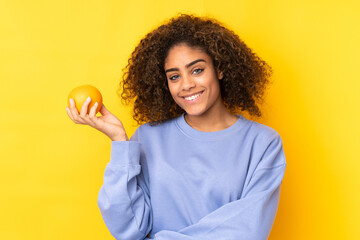 Young African American woman holding an orange over yellow background