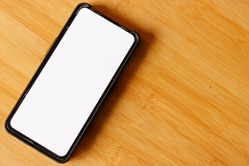 White screen smartphone on a wooden table with copy space for the graphic montage.