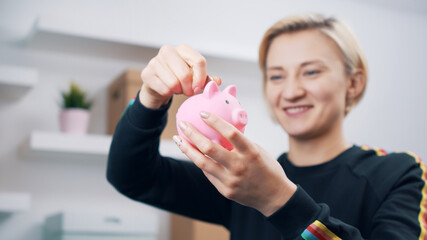Obraz na płótnie Canvas Portrait of young happy caucasian woman putting coins into the piggy bank. High quality photo