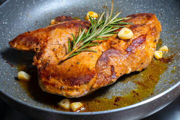 Delicious juicy pork steak seasoned with rosemary and garlic is fried in a pan.