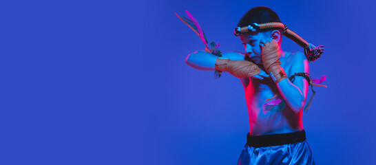 Young boy thai boxer posing over blue background in neon light.