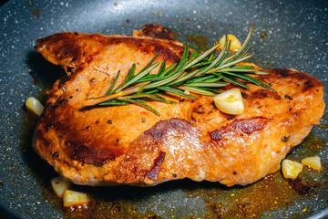Delicious juicy pork steak seasoned with rosemary and garlic is fried in a pan.