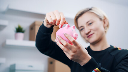 Obraz na płótnie Canvas Portrait of young happy caucasian woman putting coins into the piggy bank. High quality photo