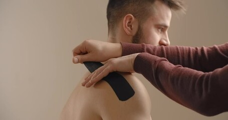 Kinesiologist sticks tapes to the shoulder of man, recovery of an athlete after injury, kinesiotherapy, 4k 60p Prores HQ 10 bit