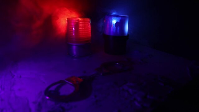 Police raid at night and you are under arrest concept. Silhouette of handcuffs with flashing red and blue police lights at foggy background. Selective focus