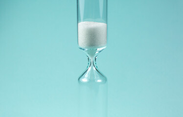 Sand clock on turquoise background. Hourglass as time passing concept. Close up photo.