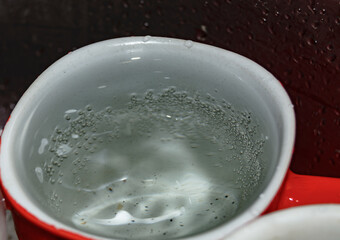 a stream of water pours into a mug with a spoon in the dish sink close-up. blurred focus