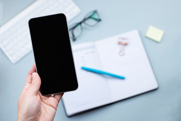 Smartphone in hand mock up over desktop with open planner and glasses. Planning, business mobile app concept