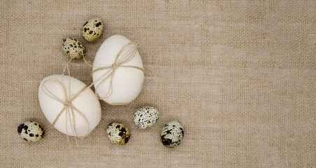Obraz na płótnie Canvas Two wooden eggs with twine bows, quail eggs on a burlap background with copy space. Concept of Happy Easter, birth. Banner.