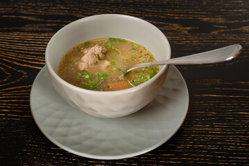 Soup with meat and herbs in a gray bowl on a dark wooden table. Chikhirtma Georgian dish.