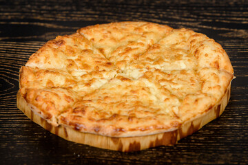 Tortilla baked with cheese on a wooden plate on a dark wooden table. Cheese pastries with a crispy crust.