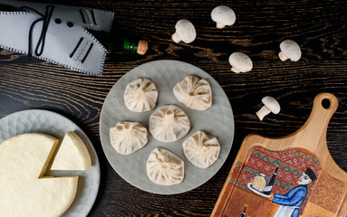 Khinkali on a gray plate, cheese on the background of a bottle in the Georgian style, mushrooms, a board with a thematic pattern on a dark wooden table. Top view