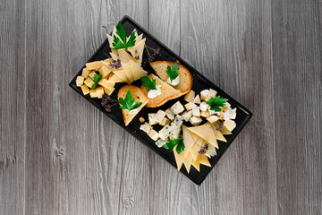 Cheese food board with delicous cheeses, walnuts. Parmesan, jam, dorblu on the black plate. Food appetizer from restaurant