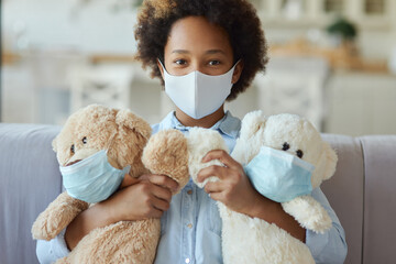 Portrait of mixed race teen girl child in protective face mask looking at camera and holding teddy bear toys wearing masks - Powered by Adobe