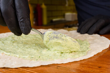 Burrito cooking process. Gloved cook spreads the pita with sauce. Mexican dish.