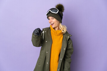 Skier Russian girl with snowboarding glasses isolated on purple background pointing front with happy expression