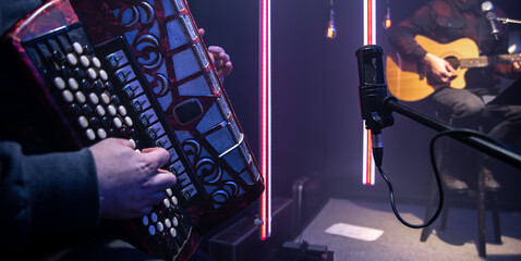 A man plays the accordion in the studio in front of a microphone.