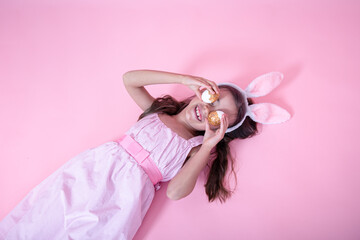 Cheerful little girl, dressed in Easter bunny ears and in a dress, is posing with Easter eggs.