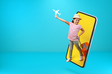 A little girl in full growth with a paper white plane and a suitcase comes out of the smartphone. Child online on a mobile phone screen with copy space.