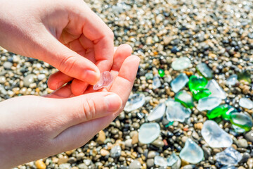 Colorful polished pieces of sea glass collected from the beach in a child hand. Beautiful close-up sea green, blue and white glass on a sea beach background.