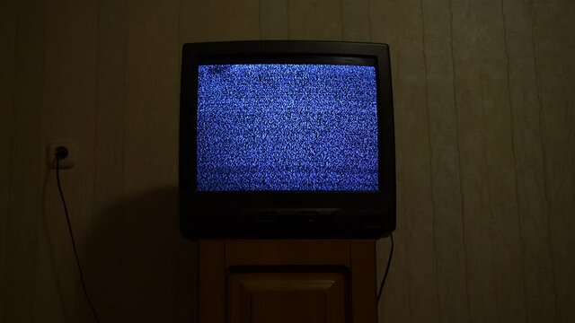 Old retro tv with glitch snowy broadcast stands on wooden bedside table