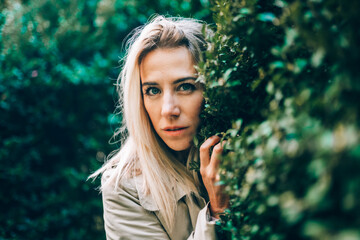 Naklejka premium Caucasian blonde woman walk in green park on sunny summer or spring day. Female wear biege trench