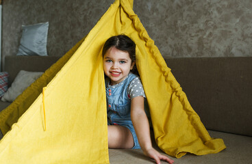 little girl playing at home on the couch hiding in a yellow teepee