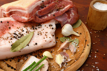 raw pork meat and lard with salt, spices and garlic on a cutting board, dark wooden background