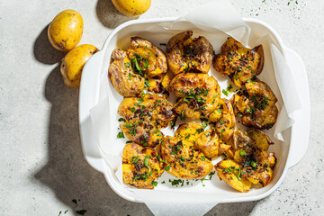 Baked smashed potatoes with herbs in white oven dish, top view.