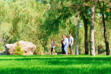 people walking and children playing in a city park on a summer day, green lawns with grass and trees, paths and benches, bright sunlight and shadows