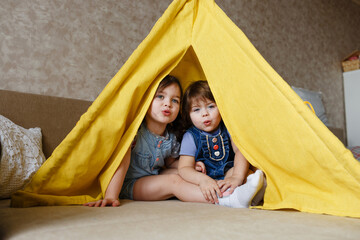 two little girls play at home in yellow in a teepee