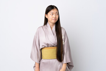 Fototapeta premium Young Chinese girl wearing kimono over isolated background having doubts while looking up