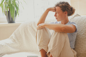 Upset depressed young brunette woman looking in distance sitting on sofa at home. Feeling anxiety, thinking about life, relationships problem, unexpected pregnancy, experiencing grief, heartbreak.
