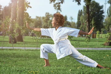 Adorable Afro American girl practicing karate on sunny day in park