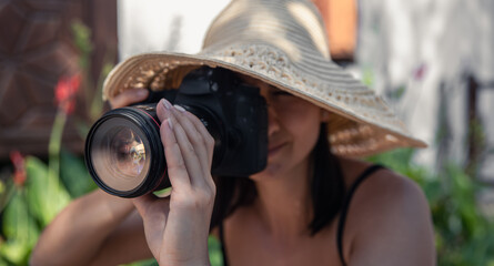 Fototapeta na wymiar A girl in a big straw hat makes a photo on a professional camera.