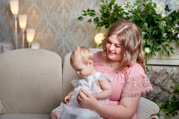 Portrait of a little blonde girl and plumb chubby mother in beautiful dress. Family in studio during photo shoot