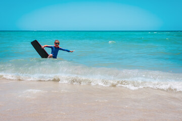Happy boy surfing on tropical beach .Active water sports for kids.