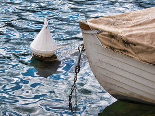 On the water, a white buoy and the bow of a small boat fixed with an anchor chain. Focus on the bow