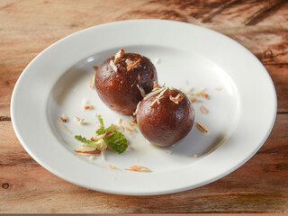 Gulab jamun traditional indian dessert,served over a white plate on a rustic wooden background, selective focus
