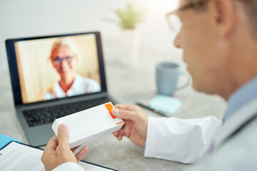 Male doctor holding medicaments and using laptop in clinic