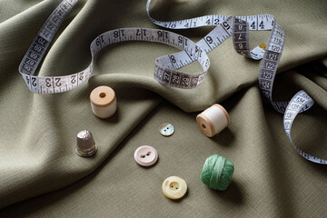 Sewing supplies lie on draped fabric, close-up. Sewing background. Spools of thread, a centimeter, scissors, a thimble, on a gray draped cloth. Atelier concept. Fashion designer. Sewing composition